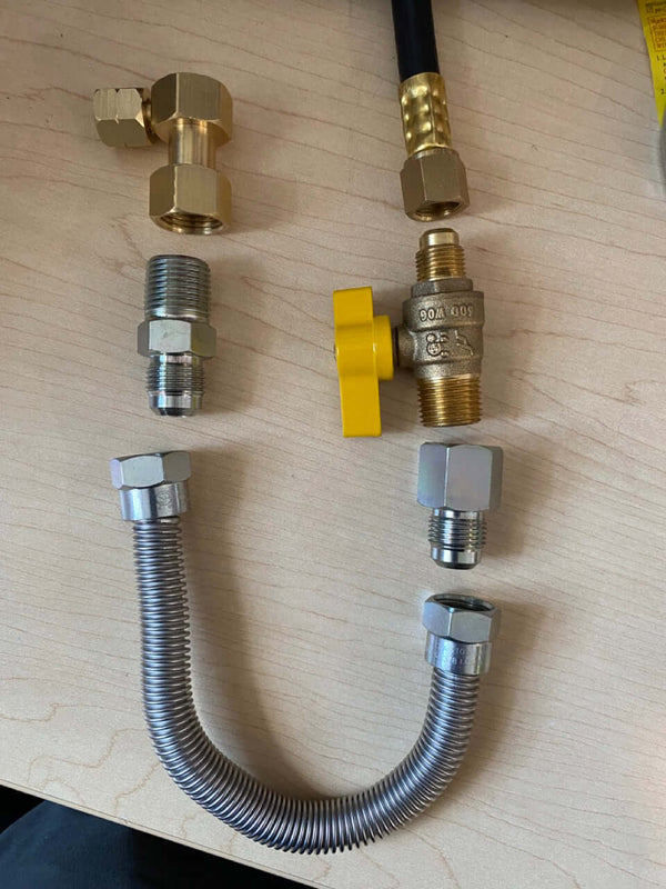 Various brass and metal connectors with a yellow valve on a wooden surface, suitable for plumbing applications.